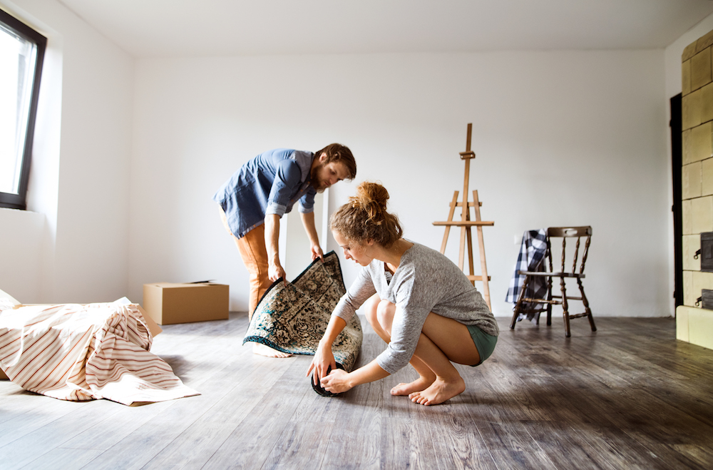 Young couple moving in new house, rolling out carpet.