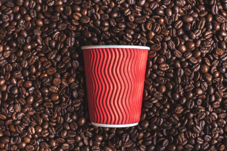 close up of red plastic cup lying on roasted coffee beans